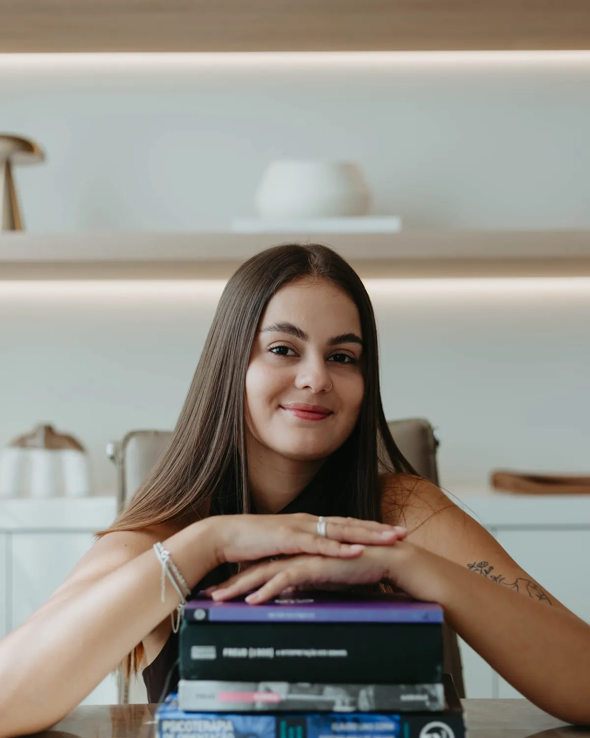 Mikaella Nunes de Souza, psicóloga, sorrindo, apoiada sobre livros de psicanálise